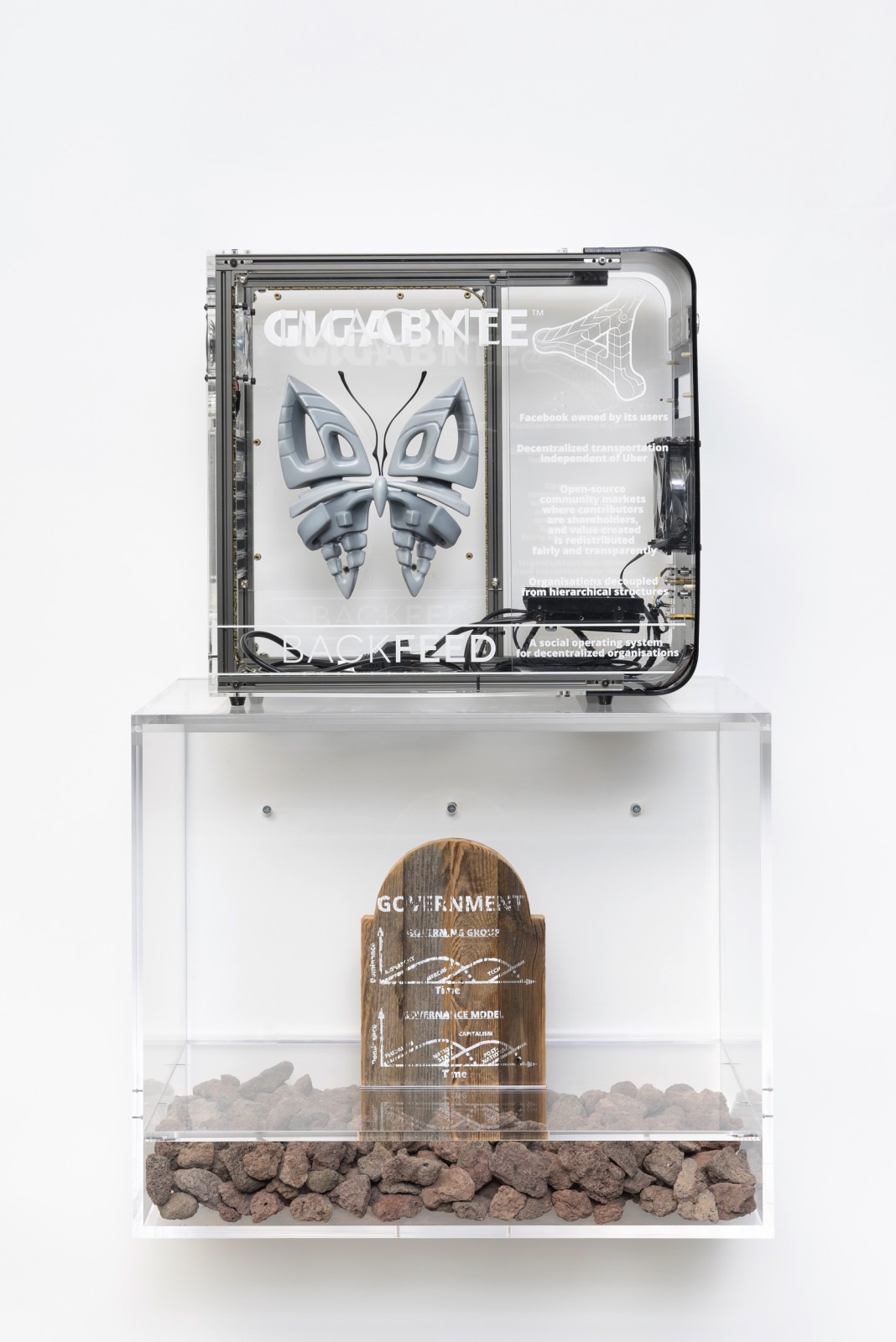 Simon Denny. <em>Blockchain Future State Fintech Gamer Case Mod Deal Toy: Backfeed x Ethereum</em>, 2016. Custom made IMAGINE butterfly, UV print on Gigabyte plexiglas computer case, screenprint on wooden tombstone, lava stones, plexiglas. Casemod: 18.11 x 19.29 x 8.27 in, Plexiplinth: 19.69 x 24.02 x 13.78 in